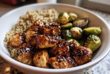 Close-up of a Maple Dijon Chicken Bowl featuring glazed chicken pieces, quinoa, and roasted Brussels sprouts in a white bowl.