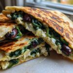 Two halves of a golden-brown Mediterranean Quesadillas, filled with wilted spinach, feta cheese, and Kalamata olives.