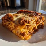 A generous slice of Million Dollar Italian Lasagna showing rich meat sauce and melted cheese layers, served on a white plate.