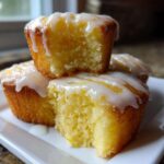 Close-up of three moist, yellow Mini Lemon Cakes Recipe topped with a thick, white lemon glaze, one cake is broken open.