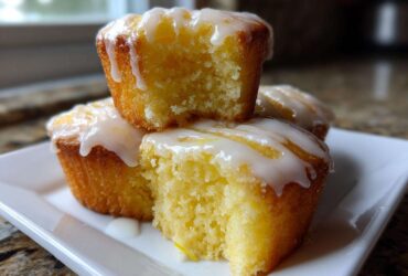 Close-up of three moist, yellow Mini Lemon Cakes Recipe topped with a thick, white lemon glaze, one cake is broken open.
