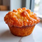 Close-up of a golden muffin topped with a thick, glistening Fluffy Orange Muffin Glaze.