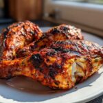 Close-up of three juicy, charred Nando's Peri Peri Chicken Copycat drumsticks on a white plate.