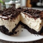 A slice removed from a rich Nobake Cheesecake Silky Sets Perfectly, showing a thick white filling, dark chocolate crust, and crumb topping.