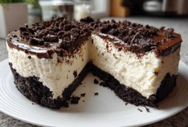 A slice removed from a rich Nobake Cheesecake Silky Sets Perfectly, showing a thick white filling, dark chocolate crust, and crumb topping.