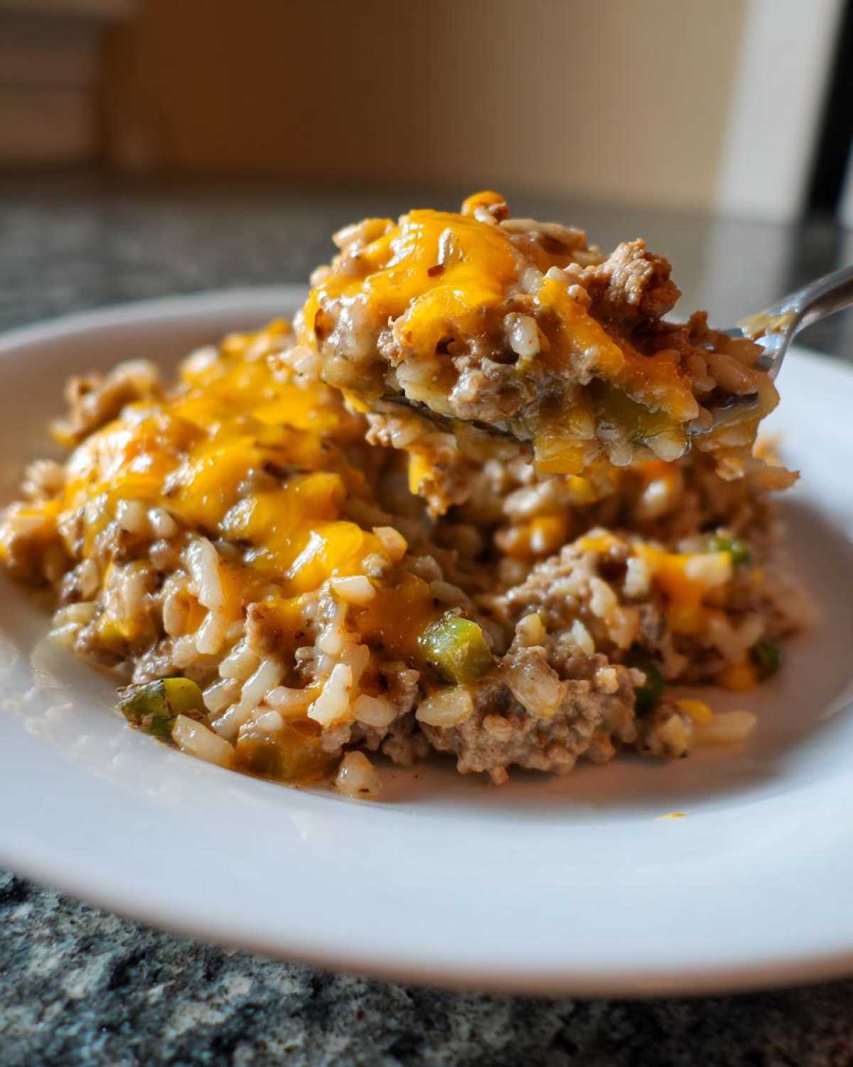 A spoonful of One Pan Ground Turkey Casserole topped with melted cheddar cheese being lifted from a white plate.