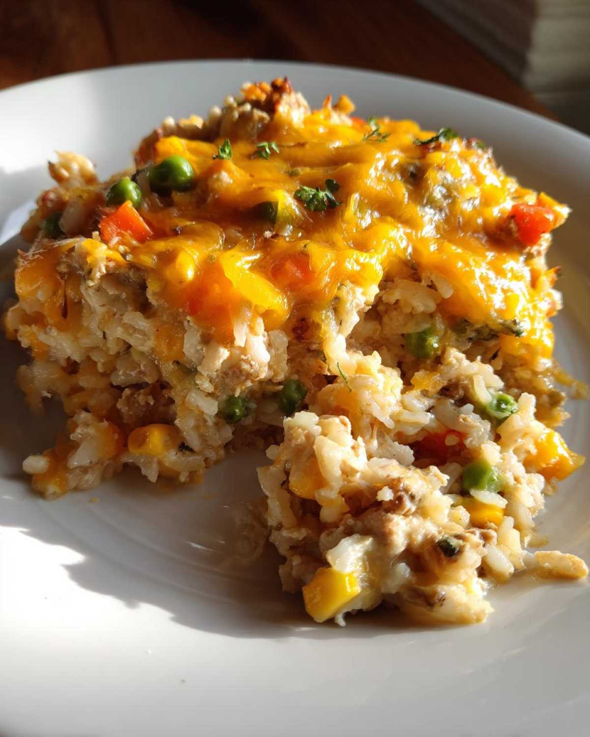 A close-up serving of One Pan Ground Turkey Casserole featuring rice, vegetables, and melted cheddar cheese on a white plate.