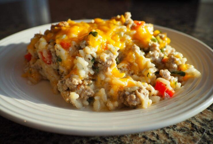 A close-up serving of One Pan Ground Turkey Casserole topped with melted cheddar cheese on a white plate.