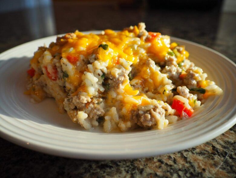 A close-up serving of One Pan Ground Turkey Casserole topped with melted cheddar cheese on a white plate.