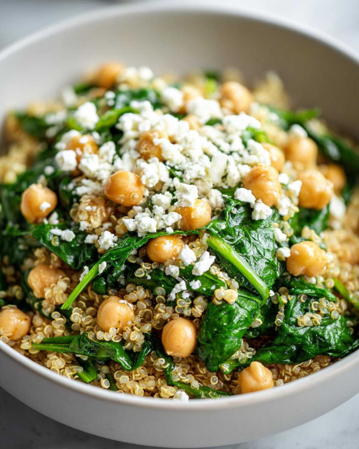 Close-up of a bowl filled with One Pot Chickpea Quinoa Recipe, topped with spinach, chickpeas, and crumbled feta cheese.