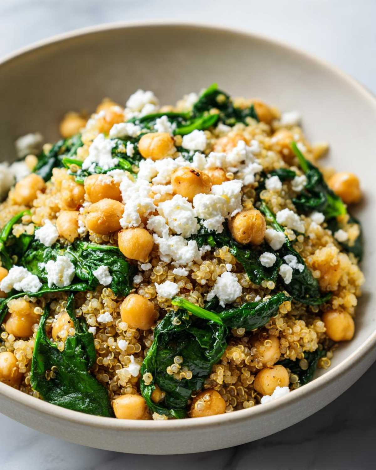 Close-up of a bowl filled with the One Pot Chickpea Quinoa Recipe, topped with spinach, chickpeas, and feta cheese.