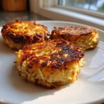 Three golden-brown, crispy Oven-Baked Cabbage Burgers served on a white plate, catching bright sunlight.