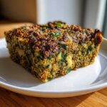 A close-up, golden-brown slice of Quinoa Lentil Spinach Casserole on a white plate.