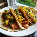 Three soft shell Salmon Tacos generously topped with bright yellow pineapple salsa and fresh cilantro.