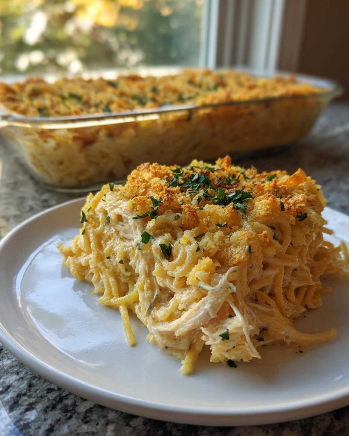 A close-up serving of creamy Chicken Spaghetti topped with golden breadcrumbs and fresh parsley, with the baking dish in the background.