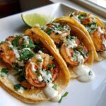 Three delicious Shrimp Tacos with Lime Crema drizzled over seasoned shrimp and topped with cilantro, served with a lime wedge.