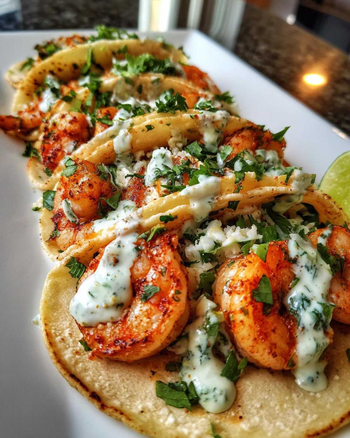 Close-up of several delicious Shrimp Tacos with Lime Crema drizzled over seasoned shrimp and topped with cilantro.