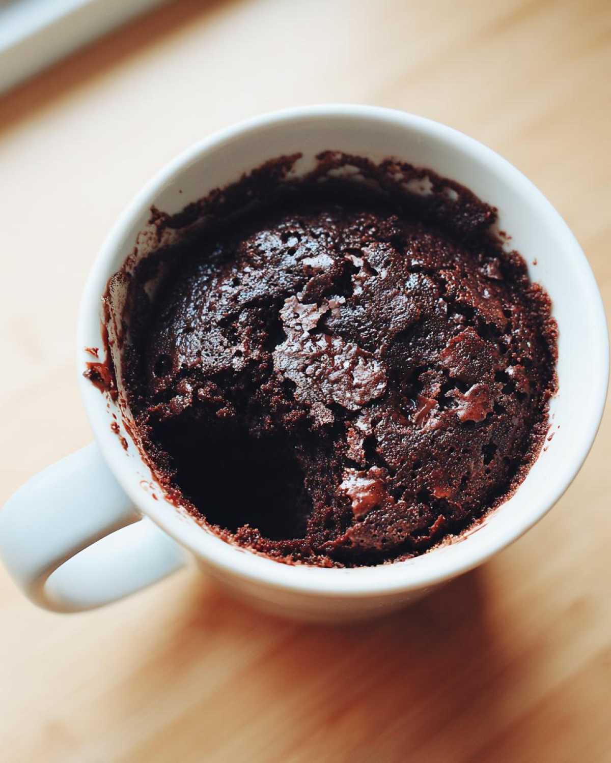 Overhead view of a rich, dark chocolate Single Serve Protein Brownie baked inside a white mug.