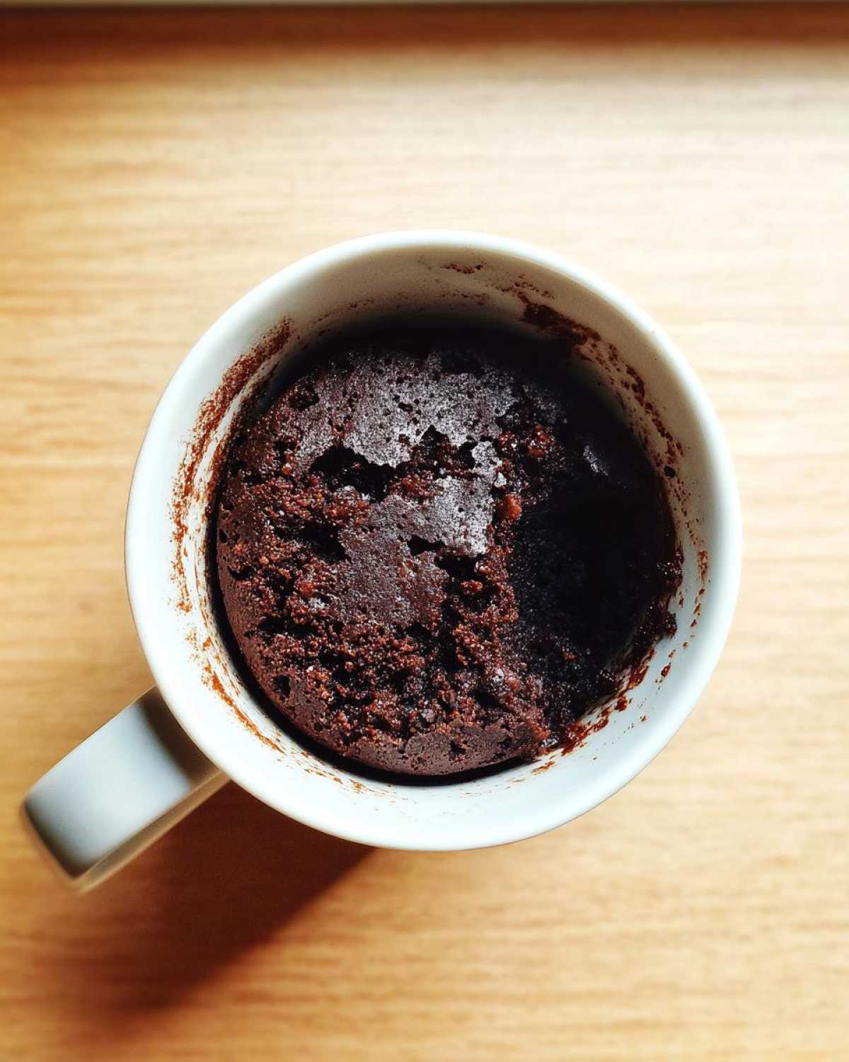 Overhead view of a rich, dark chocolate Single Serve Protein Brownie baked directly inside a white mug.