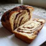 A loaf of homemade Cinnamon Swirl Bread sliced open, showing rich brown swirls inside and a glossy glaze on top.