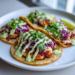 Four delicious Smash Chicken Tacos topped with red cabbage slaw, cilantro, and a creamy green sauce, served on a white plate.