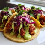 Close-up of three delicious Smash Chicken Tacos topped with red cabbage slaw and bright green avocado crema.
