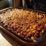 A golden-brown, baked Southwestern Black Bean Casserole featuring corn and black beans in a clear glass baking dish.