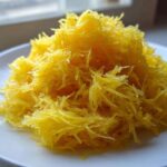A mound of bright yellow, shredded spaghetti squash recipe strands piled high on a white plate.