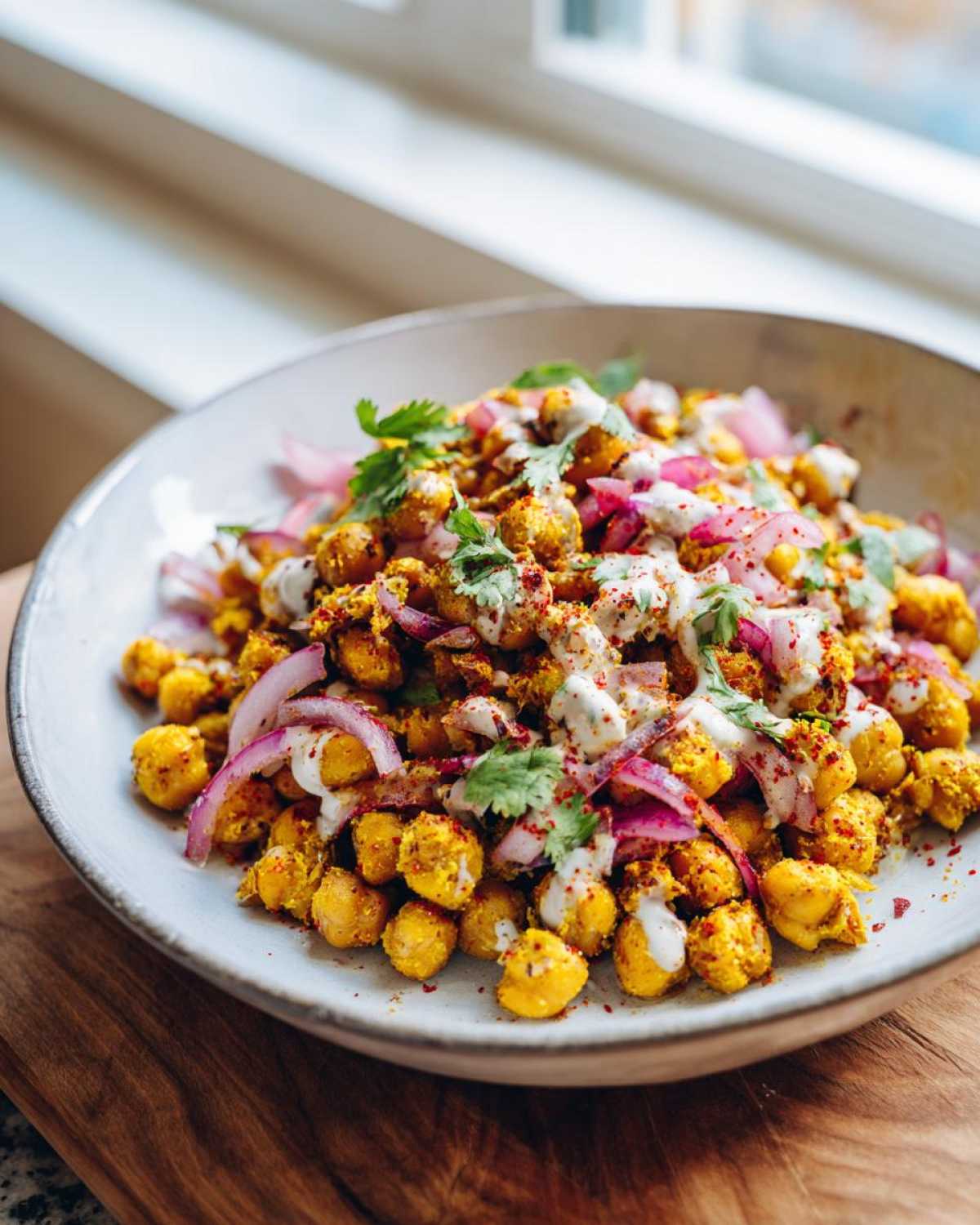 A close-up of a bowl filled with vibrant Spicy Chickpea Salad, topped with red onion, white sauce, and cilantro.