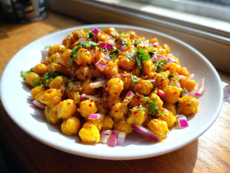 Close-up of a vibrant Spicy Chickpea Salad tossed with red onion and cilantro on a white plate.