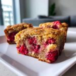 Three squares of moist Strawberry Blondies One Bowl dessert featuring bright pink embedded strawberries on a white plate.