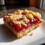 A close-up of a single serving of Strawberry Shortbread Bars Summer Delight with a thick strawberry filling and crumb topping.