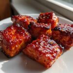 Five glistening, caramelized Sweet Chili Lime Salmon Bites stacked on a white plate, catching bright sunlight.