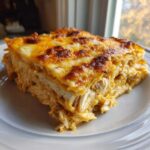 A thick, layered slice of Texas King Ranch Chicken Casserole topped with melted, browned cheese on a white plate.