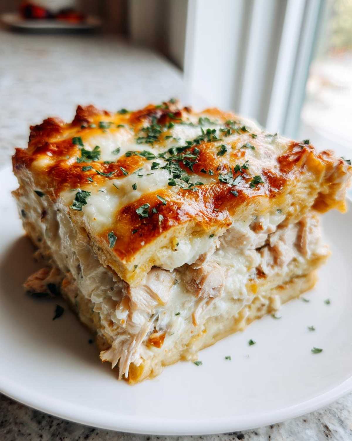 A close-up of a thick, layered slice of Texas King Ranch Chicken Casserole topped with melted, browned cheese and parsley.