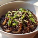 Close-up of Vegan Korean Bulgogi Lentils served in a white bowl, topped with sesame seeds and sliced green onions.