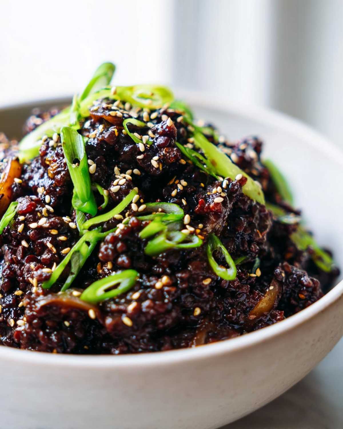 Close-up of rich, dark Vegan Korean Bulgogi Lentils topped with sesame seeds and sliced green onions.