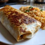 A perfectly grilled Vegetarian Bean Cheese Burrito served next to a side of Mexican rice on a white plate.