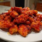 A pile of crispy chicken pieces coated in glossy, vibrant red Very Affordable Sweet Chili Chicken sauce on a white plate.