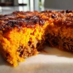 A close-up, cross-section view of the Whole30 BBQ Chicken Casserole showing the bright orange sweet potato topping over shredded BBQ chicken.
