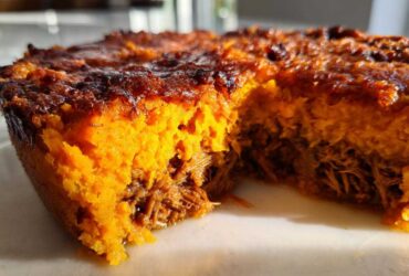 A close-up, cross-section view of the Whole30 BBQ Chicken Casserole showing the bright orange sweet potato topping over shredded BBQ chicken.