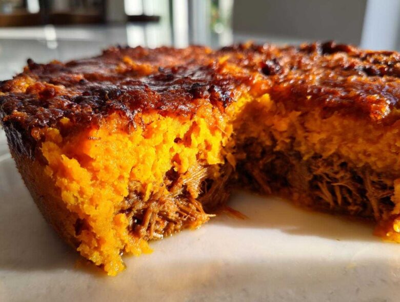 A close-up, cross-section view of the Whole30 BBQ Chicken Casserole showing the bright orange sweet potato topping over shredded BBQ chicken.