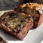 A close-up of a thick slice of moist Banana Bread Chocolate Chip next to the main loaf.