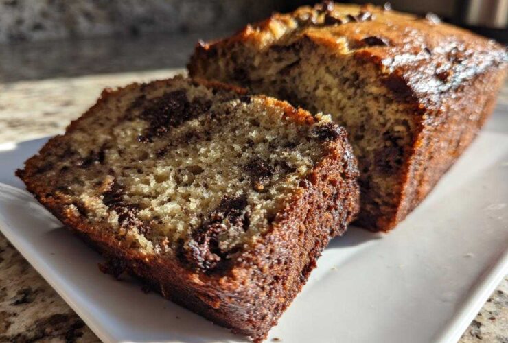 A close-up of a thick slice of moist Banana Bread Chocolate Chip next to the main loaf.