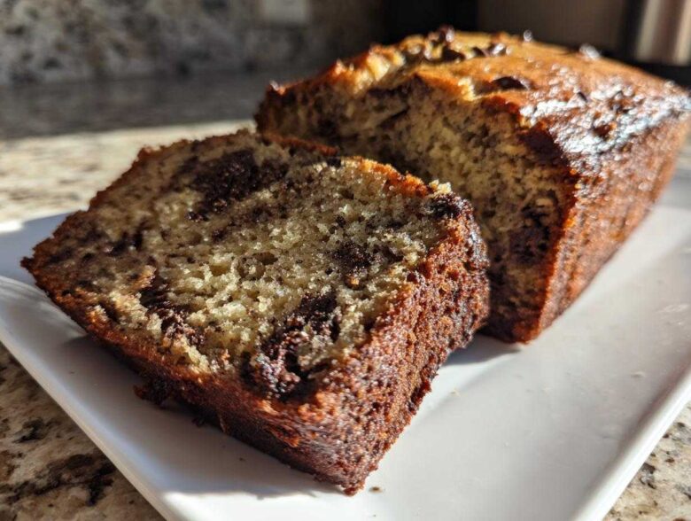 A close-up of a thick slice of moist Banana Bread Chocolate Chip next to the main loaf.