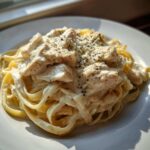 A close-up, appetizing shot of Creamy Chicken Fettuccine Alfredo pasta topped with grated cheese and black pepper.