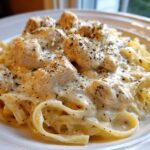 A close-up shot of a serving of Creamy Chicken Fettuccine Alfredo, featuring pasta coated in rich white sauce and topped with seasoned chicken pieces.