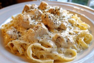A close-up shot of a serving of Creamy Chicken Fettuccine Alfredo, featuring pasta coated in rich white sauce and topped with seasoned chicken pieces.