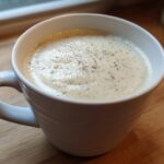 A white mug filled with hot, creamy garlic soup, topped with pepper, ready to eat.