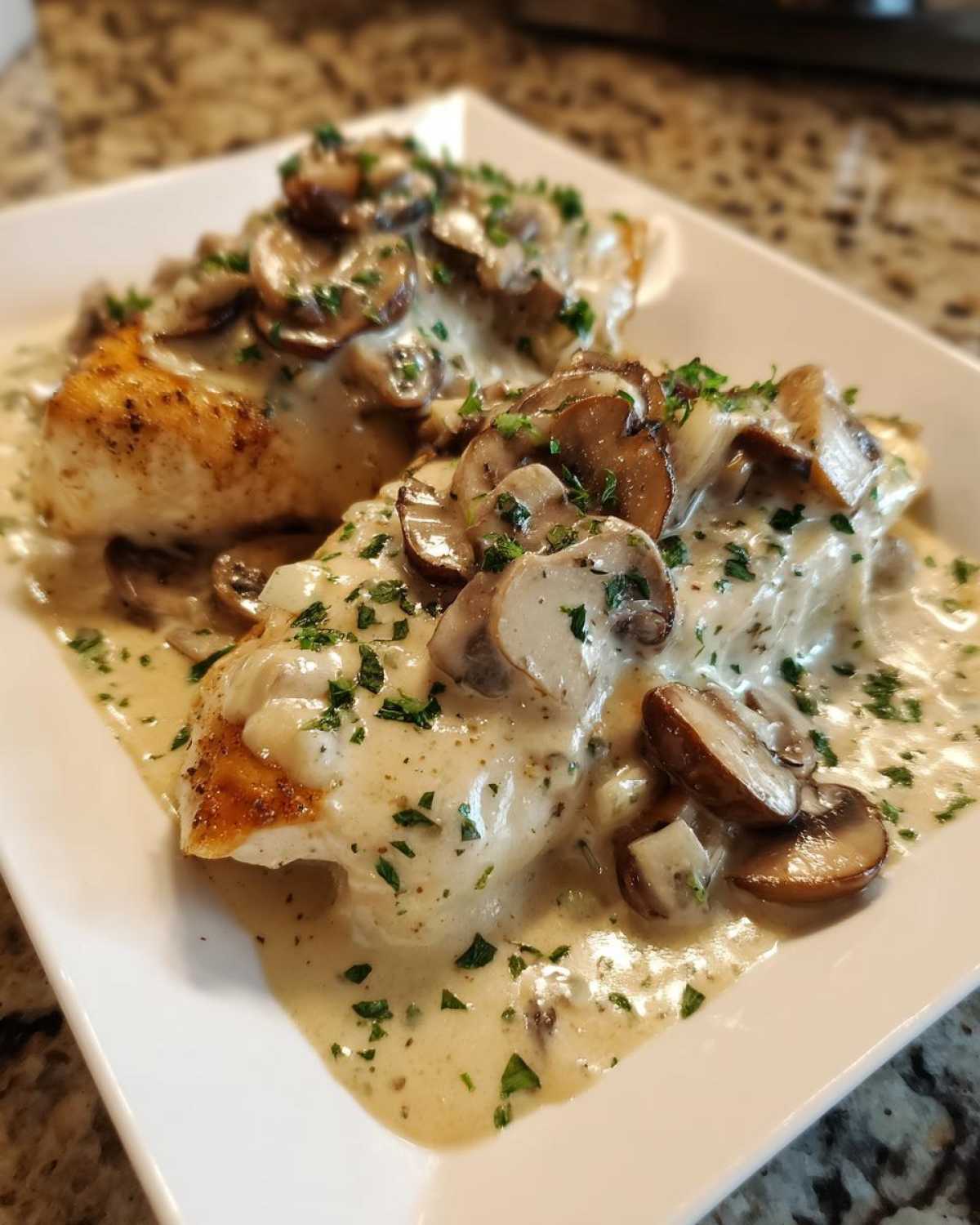 Two pieces of seared chicken breast generously covered in a creamy mushroom sauce and garnished with parsley, representing Creamy Smothered Chicken.